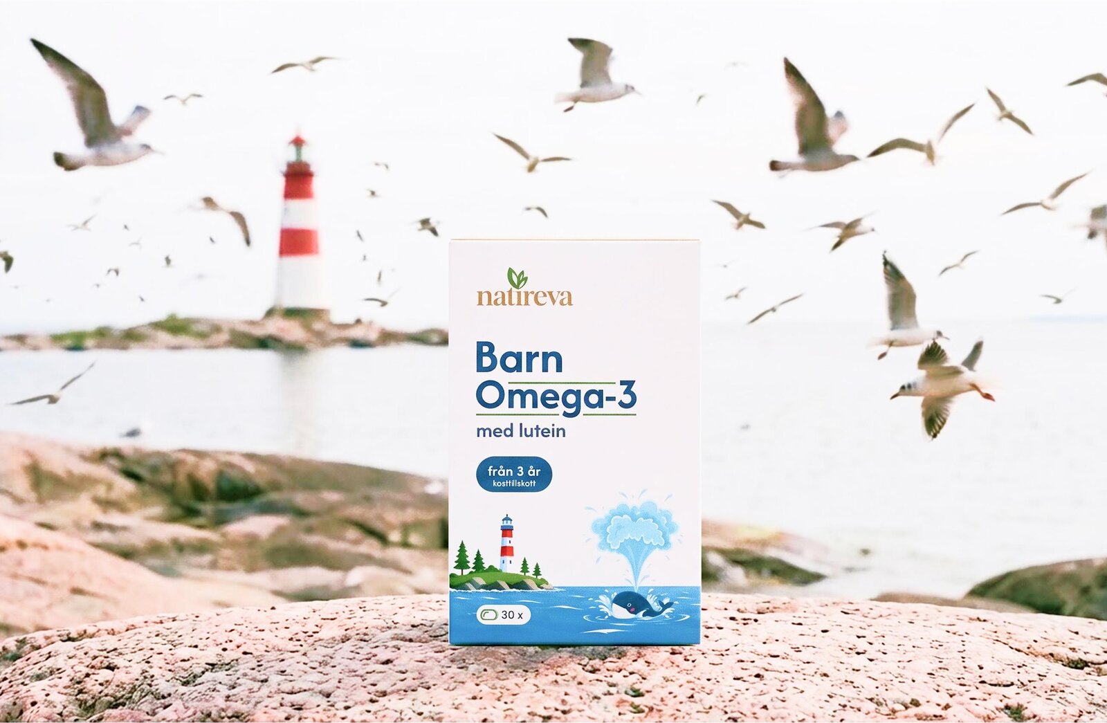 Barn Omega-3 med lutein pack standing on coastal rocks by a striped lighthouse